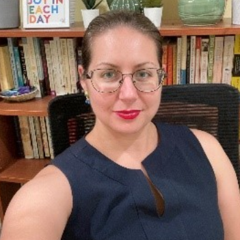 A woman with glasses sitting in front of a bookshelf.