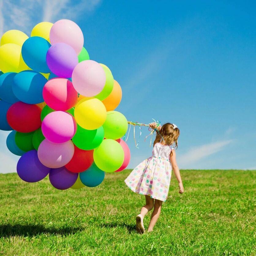 A girl holding balloons in the grass.