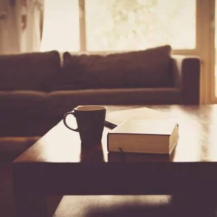 A coffee mug and book on the table in front of a window.